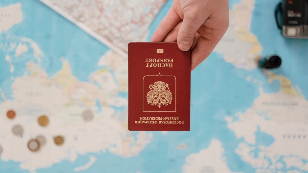 A hand holding a Russian passport above a travel-themed map, capturing world travel concepts.